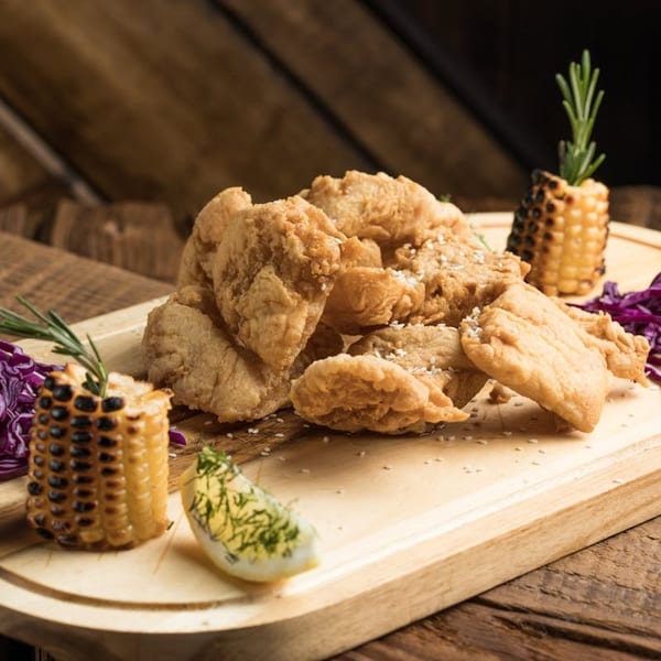 Crispy fried chicken pieces, grilled corn, red cabbage, and a hard-boiled egg on a wooden board.