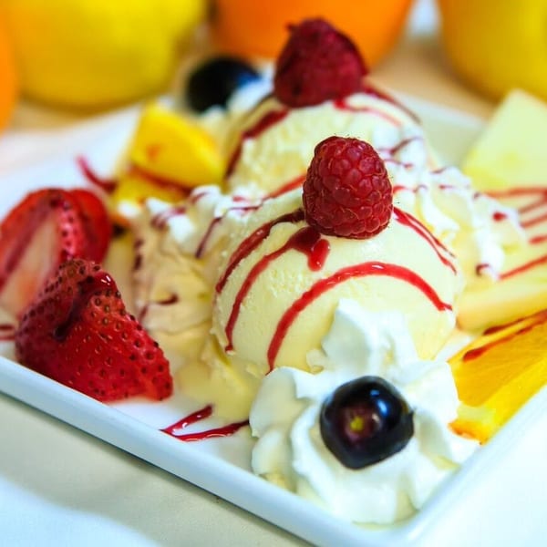 Vanilla ice cream scoops with raspberry, strawberry, whipped cream, and fruit slices.