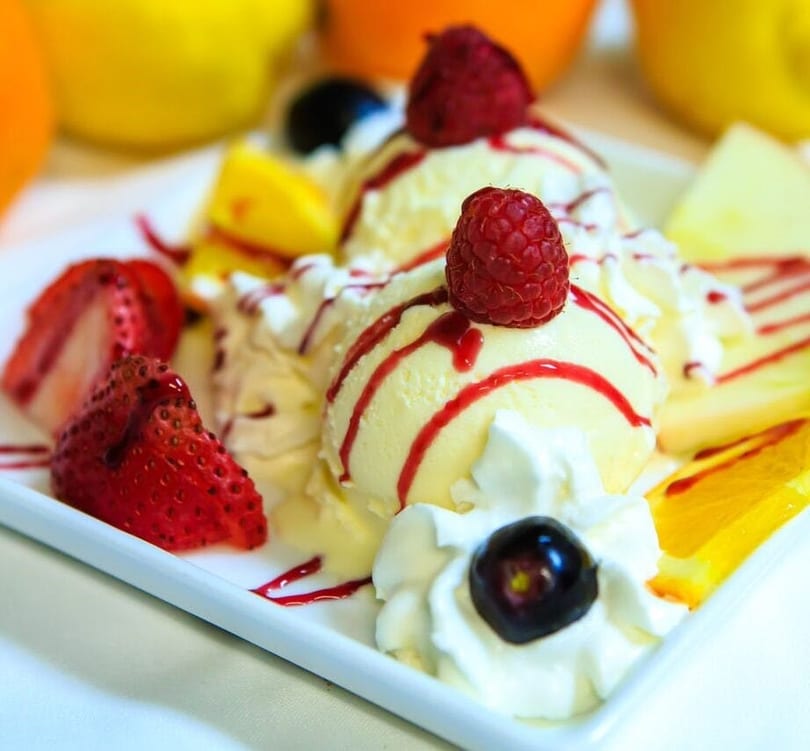 Vanilla ice cream scoops with raspberry, strawberry, whipped cream, and fruit slices.
