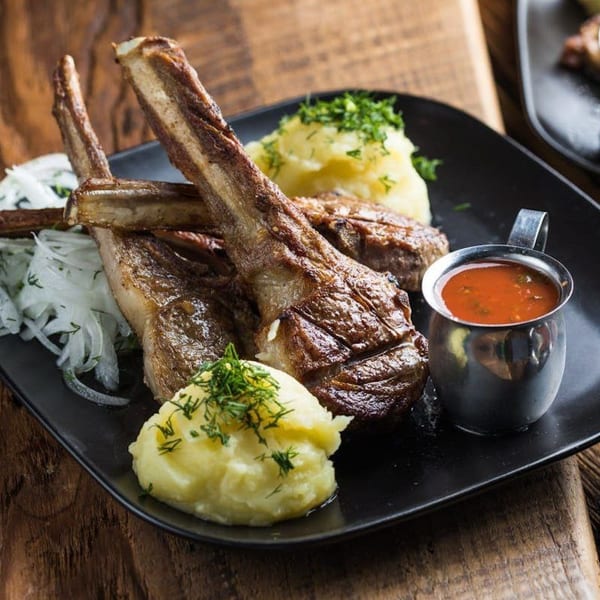 Grilled lamb chops with mashed potatoes, sliced onions, and a side of red sauce.