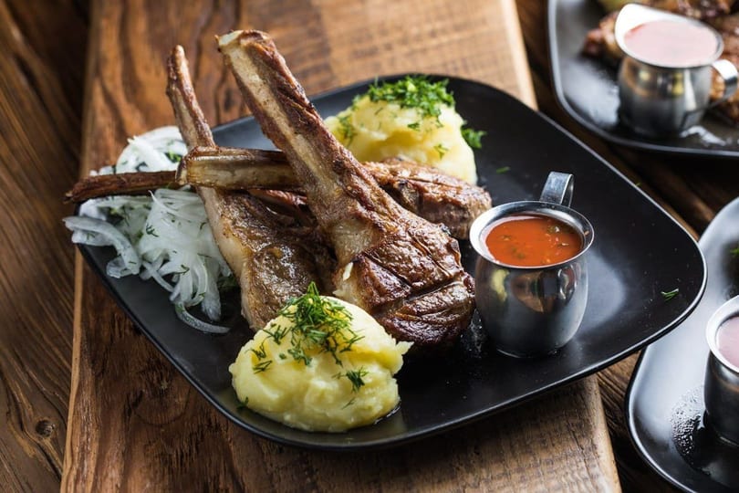 Grilled lamb chops with mashed potatoes, sliced onions, and a side of red sauce.
