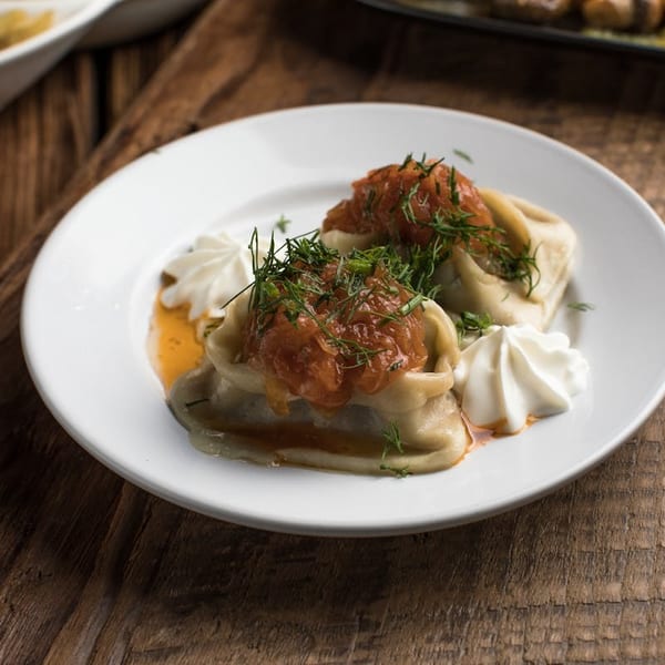 Two dumplings topped with red sauce and dill, garnished with whipped cream on a white plate.