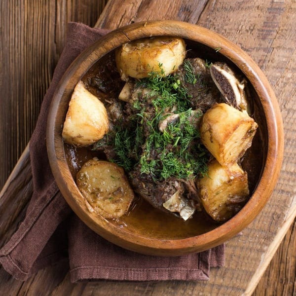 Hearty stew with meat, potatoes, and fresh dill in a wooden bowl on a rustic table.